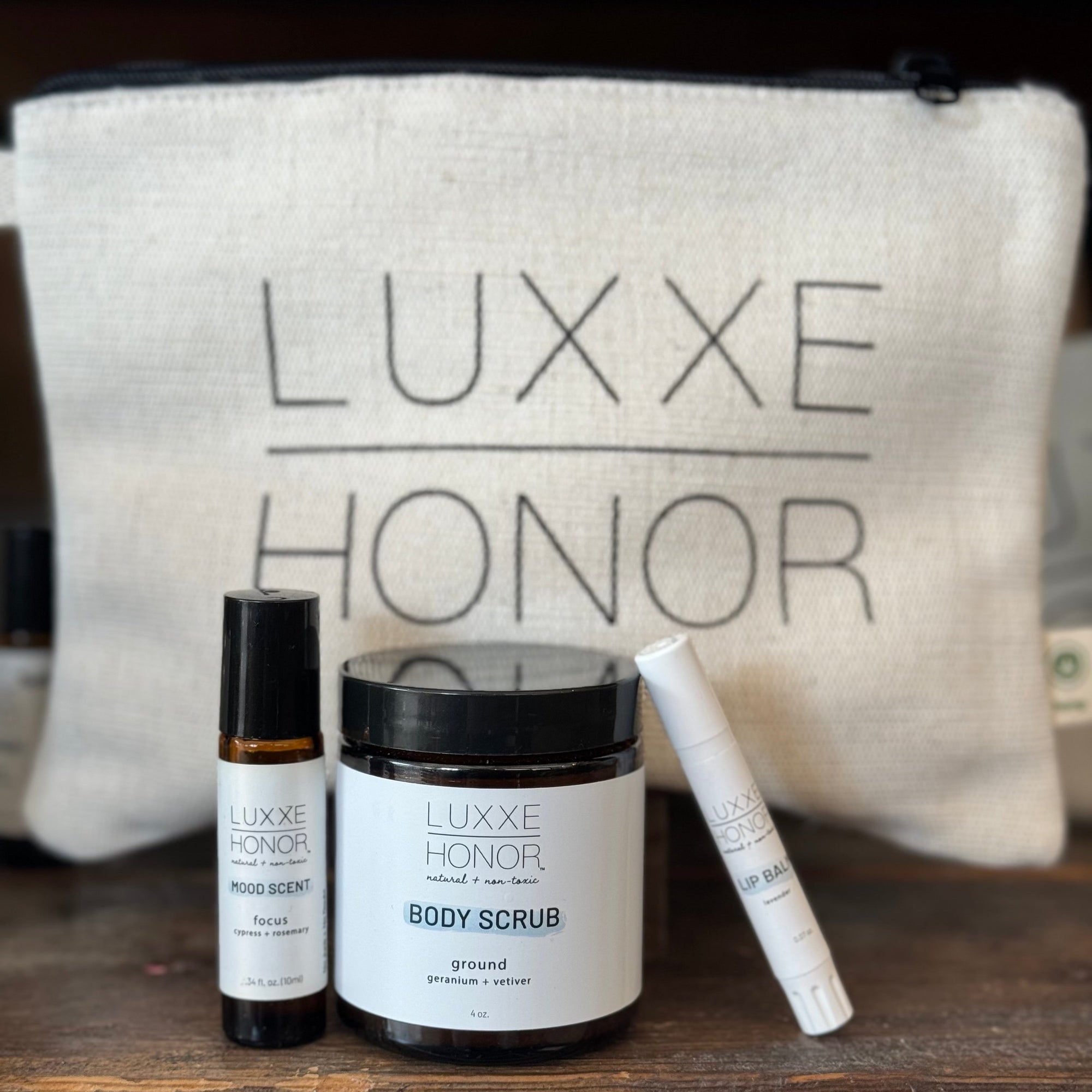 Three Luxxe Honor beauty products—mood scent, lip balm, and body scrub—rest on a wooden surface.  The labels list ingredients and sizes.
